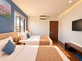 Una camera d'albergo con due letti, una TV, una porta in legno e una finestra vista edifici.