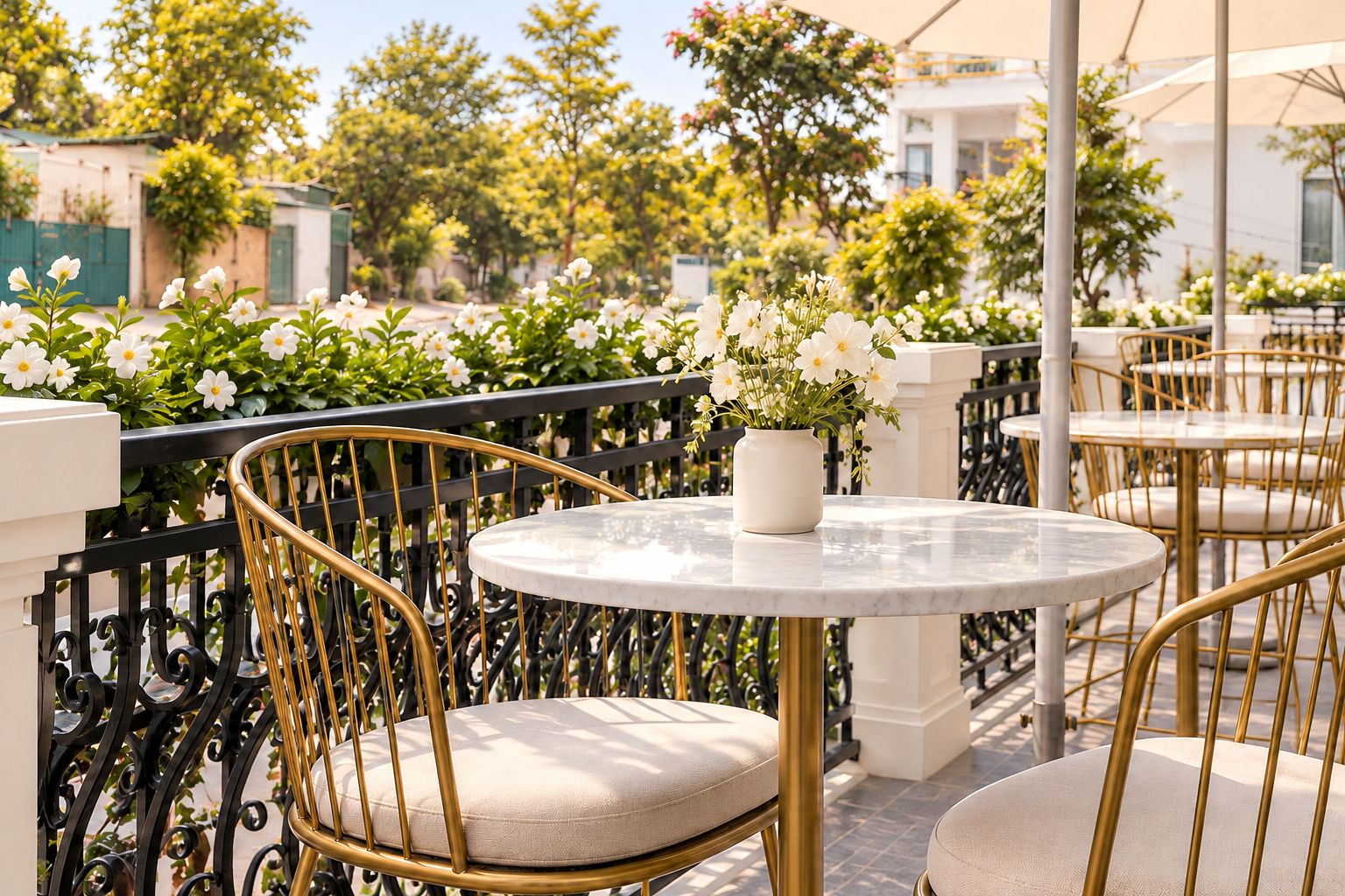 A terrace with round tables and chairs, a white vase with flowers, and a black wrought iron railing.