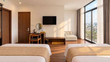 A hotel room with two beds, a desk with a chair, a television, and a view of the city through large windows.