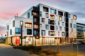 Un hôtel à plusieurs étages doté de balcons, d’un parking clôturé et d’une enseigne rouge bien visible.