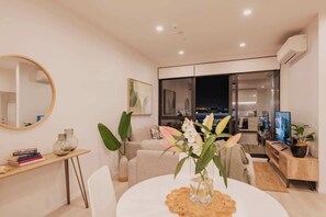 Un salon moderne comprenant une table à manger, un canapé, un téléviseur et une grande fenêtre.