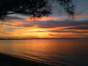 A sunset over a calm body of water with a silhouette of land in the distance.