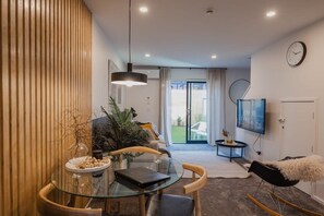 Relax in this stylish living space with a glass dining table, comfortable sofa, and a cozy reading nook.