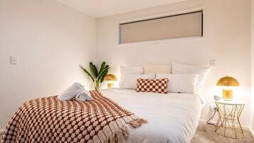 Ein Hotelzimmer mit einem Bett, einer karierten Tagesdecke, einer Pflanze, zwei Nachttischlampen und einer Wandleuchte.