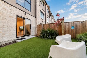 A modern building with a brick facade, a glass door entrance, and a well-maintained lawn with two white plastic chairs.