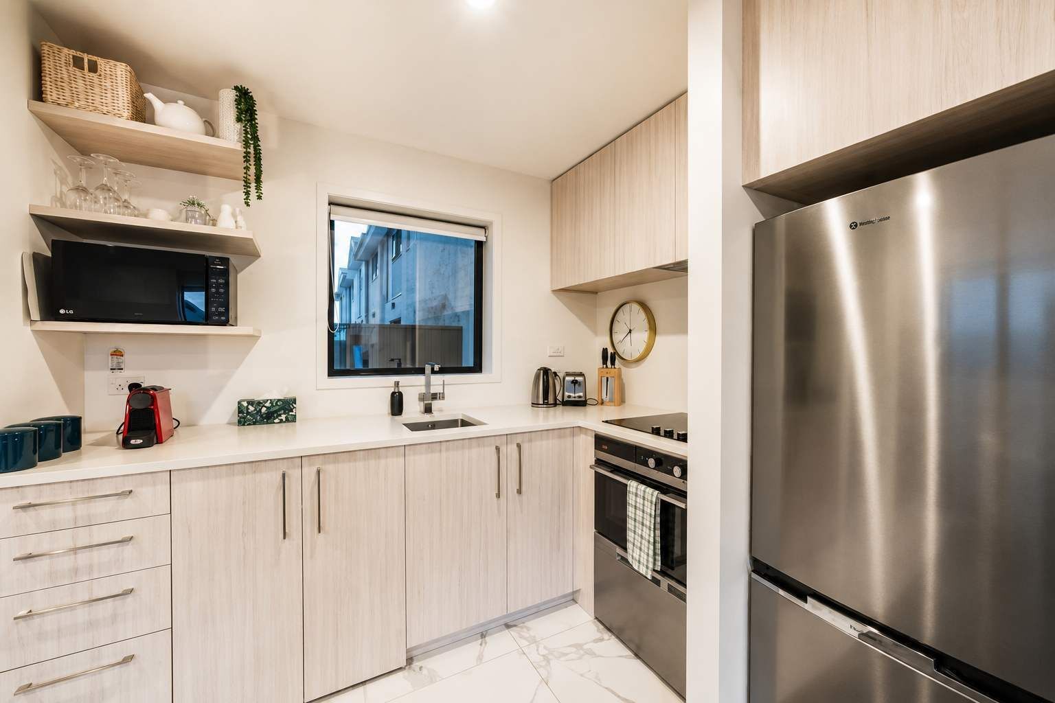 Una cocina moderna con un refrigerador de acero inoxidable, un microondas, una cafetera y una ventana con vistas a edificios.