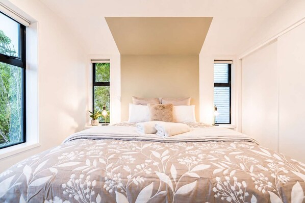 A bedroom with a large bed, two windows, and a view of greenery outside.