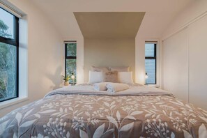 Une chambre avec un grand lit, deux fenêtres et une vue sur les arbres.