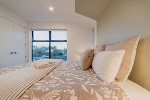 Une chambre avec une grande fenêtre, un lit recouvert d’une literie à motifs floraux et une vue sur l’extérieur.