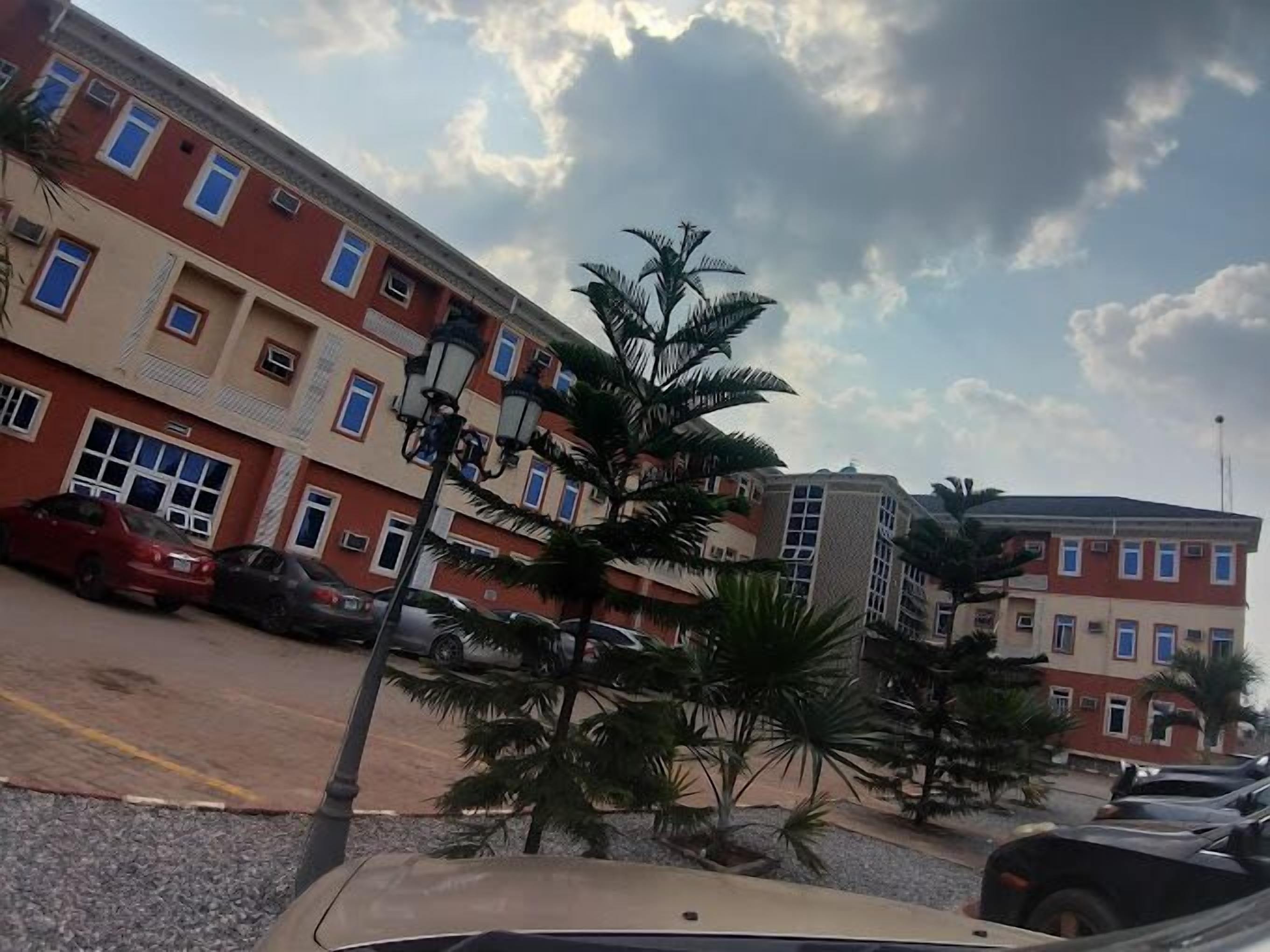 A multi-story building with red and beige exterior walls, several windows, and a parking lot with cars.