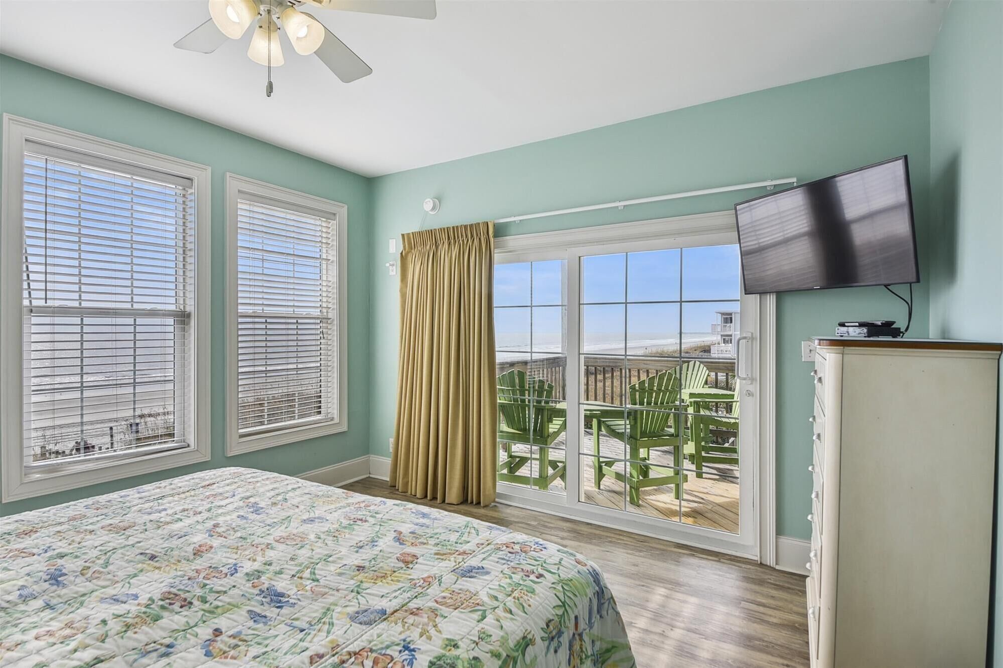 Une chambre à coucher avec un lit, un ventilateur de plafond, une télévision et un balcon équipé de chaises.