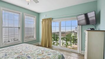 Une chambre à coucher avec un lit, un ventilateur de plafond, une télévision et un balcon équipé de chaises.