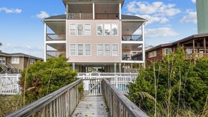 A multi-story building with a wooden deck leading to the entrance, surrounded by greenery.