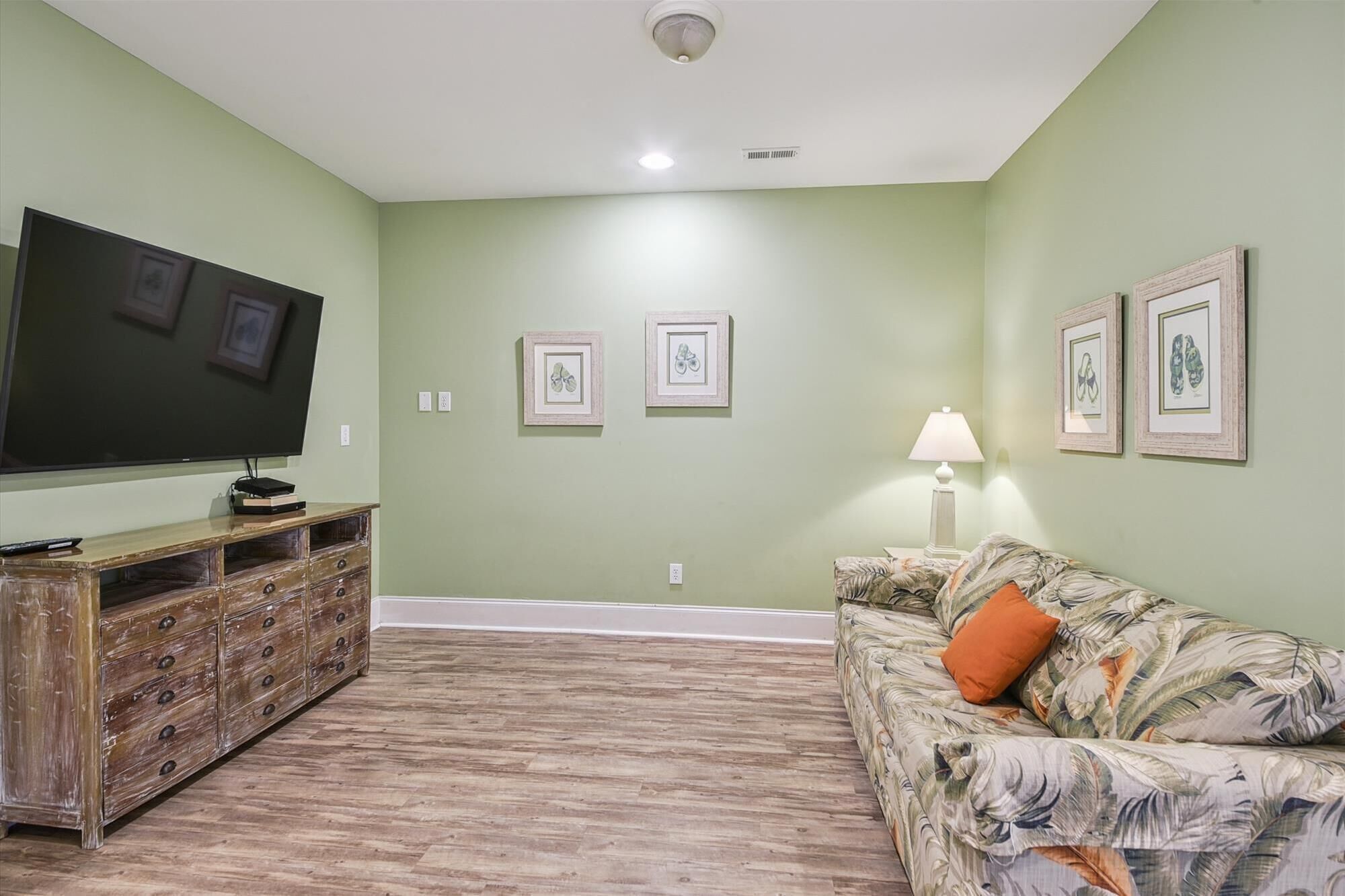 A living room with a flat-screen TV, wooden entertainment center, floral sofa, and framed artwork on the walls.