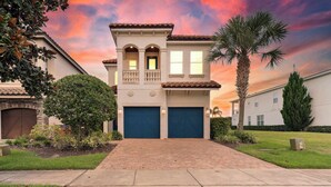 A two-story house with a brick driveway, a palm tree, and a sunset sky. - Spacious home w/ themed rooms, pool & game room (Kissimmee)