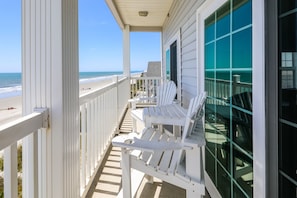 A balcony with white Adirondack chairs overlooking a beach.