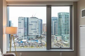 A view from a window with a lamp on the left, overlooking a cityscape with modern buildings and a parking lot.