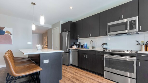 A modern kitchen with dark cabinets, stainless steel appliances, and a central island with bar stools.