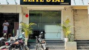 A building with a sign for "HOTEL ELITE STAY" and an AC room. There are motorcycles parked in front and potted plants near the entrance. - Hotel Elite Stay (Pune)