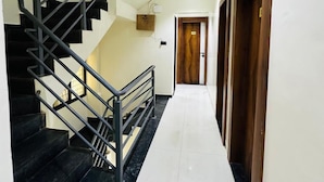 A hallway with a black staircase, white walls, and a wooden door at the end. - Hotel Elite Stay (Pune)