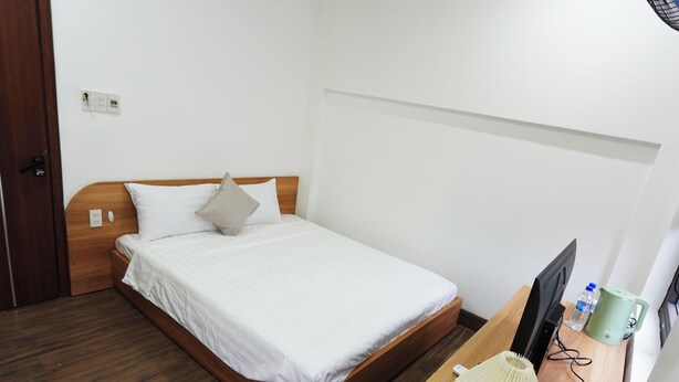 A neatly made bed with white bedding and a wooden headboard in a room with a wooden floor. - Smile Homestay (Hue)