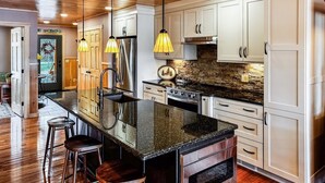 A modern kitchen with white cabinets, a granite island, stainless steel appliances, and pendant lighting. - Townhome O2 - Luxury Waterfront Home on 4th Lake (Inlet)