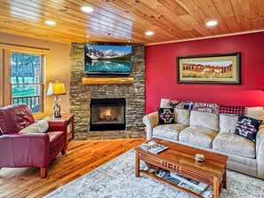 Un salon chaleureux avec une cheminée en pierre, un téléviseur fixé au mur et un mur d’accent de couleur rouge.