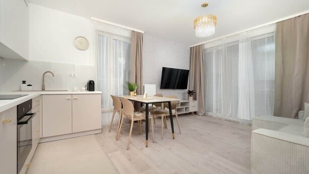 A modern kitchen with a dining area, a flat-screen TV, and a chandelier.