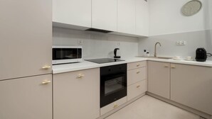 A modern kitchen with white cabinets, a black microwave, a coffee machine, and a sink.