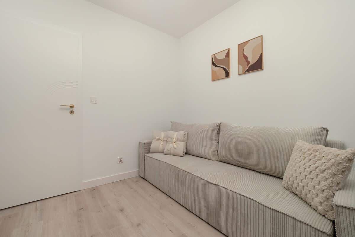 A minimalist room with a beige sofa, two wall-mounted abstract paintings, and a wooden floor.