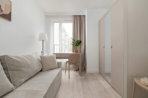 Un salon moderne et minimaliste, avec un canapé, un bureau et une plante en pot.