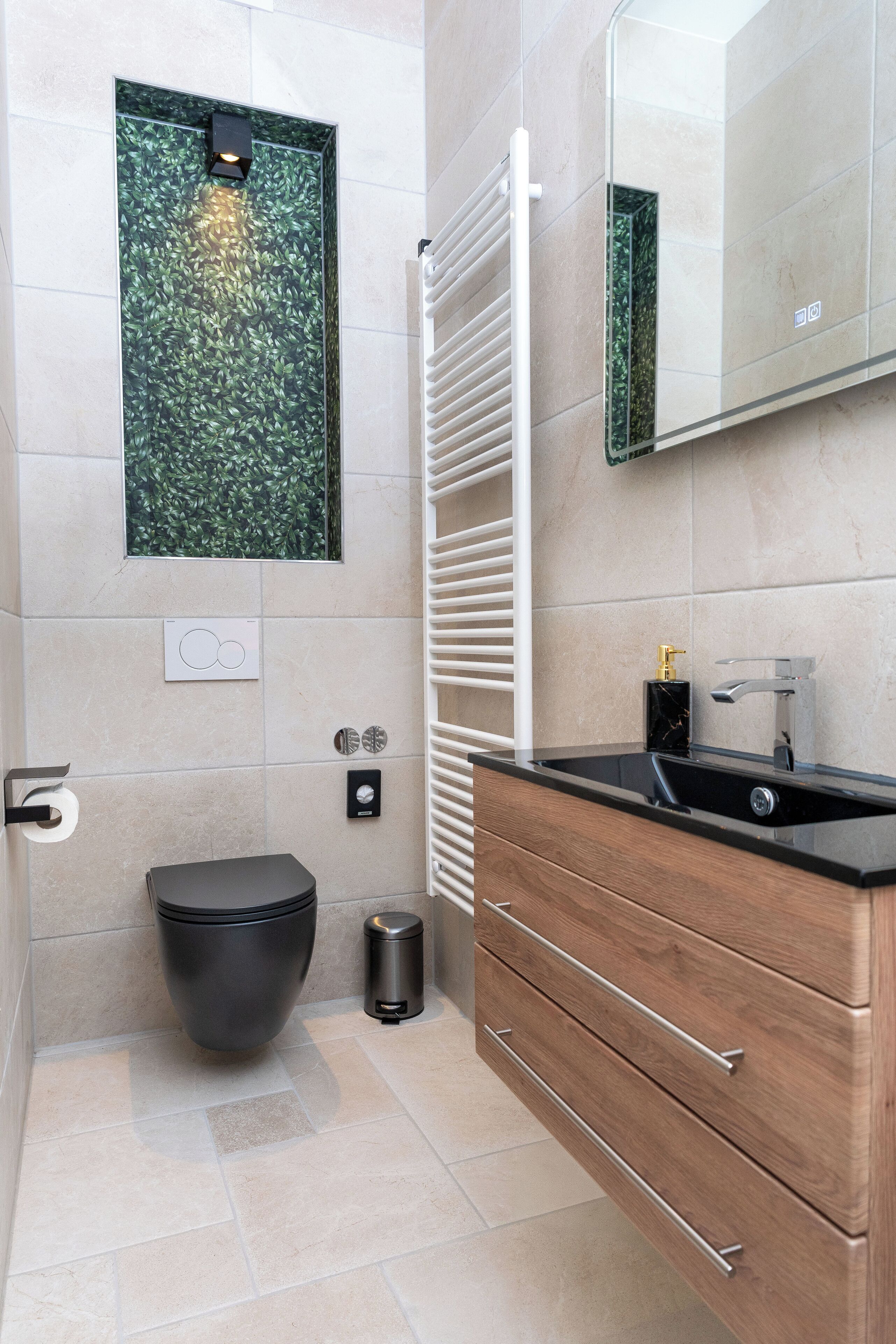 A modern bathroom with a black toilet, a wooden vanity with a black sink, a mirror, and a green leaf-patterned wall decoration.