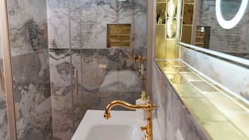 Een badkamer met marmeren wanden, een gouden kraan en een grote spiegel.