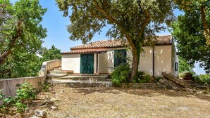 Ein Haus mit Ziegeldach, einer Steintreppe, die zum Eingang führt, und einem Garten mit verschiedenen Pflanzen und Bäumen.