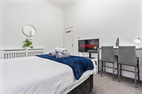 Une chambre d’hôtel moderne avec un grand lit, un bureau équipé d’un ordinateur, une télévision et une petite plante.