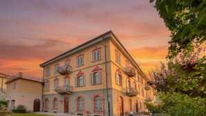 A multi-story building with balconies, arched windows, and a well-maintained lawn. - Sunny Penthouse With Mountain View (Oulx)