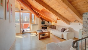 A loft-style room with a sloped ceiling, a sofa, a coffee table, and a television. - Sunny Penthouse With Mountain View (Oulx)