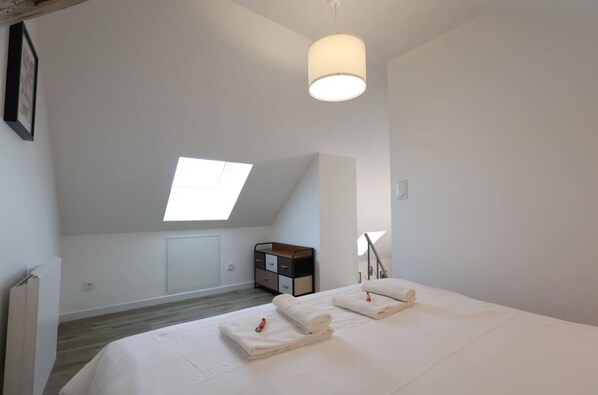 Une chambre avec un puits de lumière, un lit avec des serviettes soigneusement pliées, une table de chevet et une petite armoire.