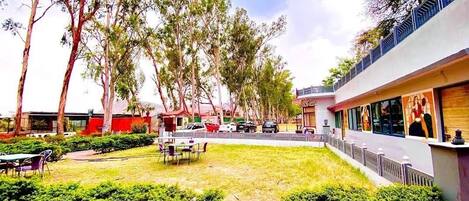 A courtyard with a dining area, surrounded by trees and a building with large windows.