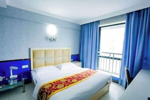 Ett hotellrum med en säng, ett sängbord, en lampa och ett fönster med gardiner.