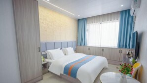 A hotel room with a bed, a bedside table, a TV, a window with curtains, a small table with a vase, and a chair. - Shuangyong Hotel (Changsha)