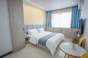 Ett hotellrum med en säng, ett sängbord, en tv, ett fönster med gardiner, ett litet bord med en vas och en stol.