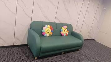 A green sofa with two colorful flower-shaped pillows against a marble wall.