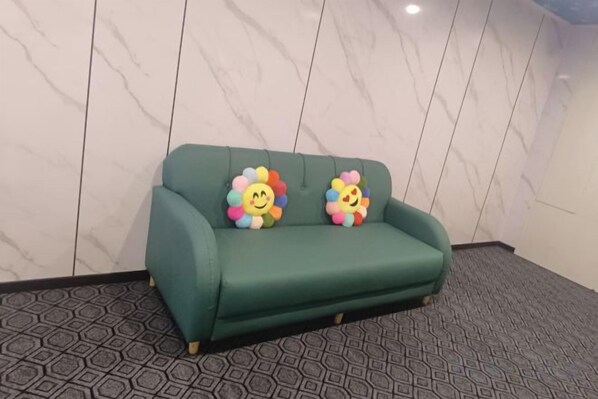 A green sofa with two colorful flower-shaped pillows against a marble wall.