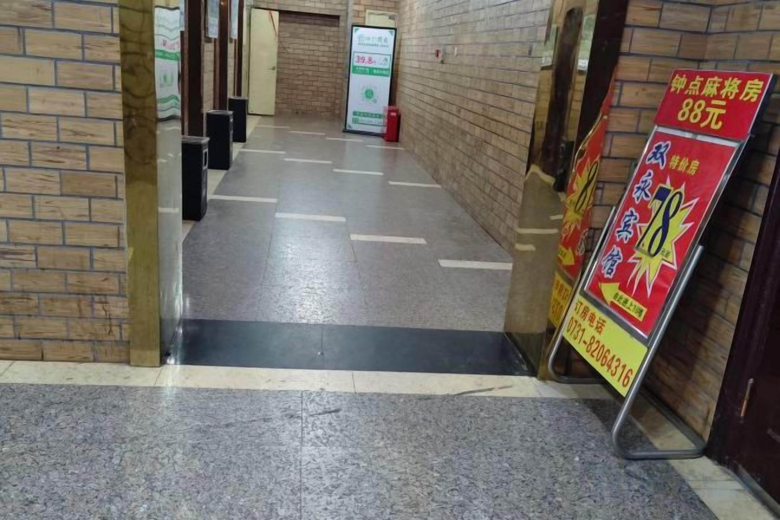 A hallway with a tiled floor, a brick wall on the left, and a signboard on the right.