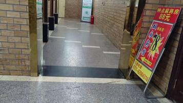 A hallway with a tiled floor, a brick wall on the left, and a signboard on the right.