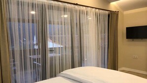 A hotel room with a bed, a TV mounted on the wall, and a window with sheer curtains. - Garden House Uzungöl (Çaykara)