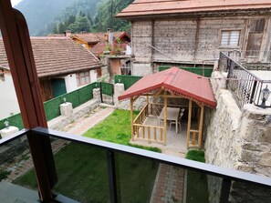 A courtyard with a wooden pergola, a stone wall, and a view of traditional houses with red-tiled roofs. - Garden House Uzungöl (Çaykara)