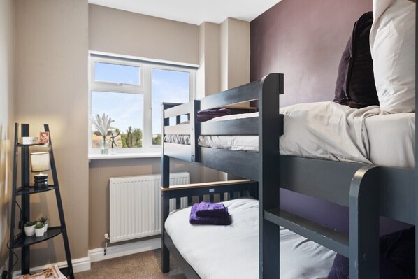 Ein Schlafsaalzimmer mit einem Fenster, Heizkörper und einem schwarzen Regal mit Gegenständen.