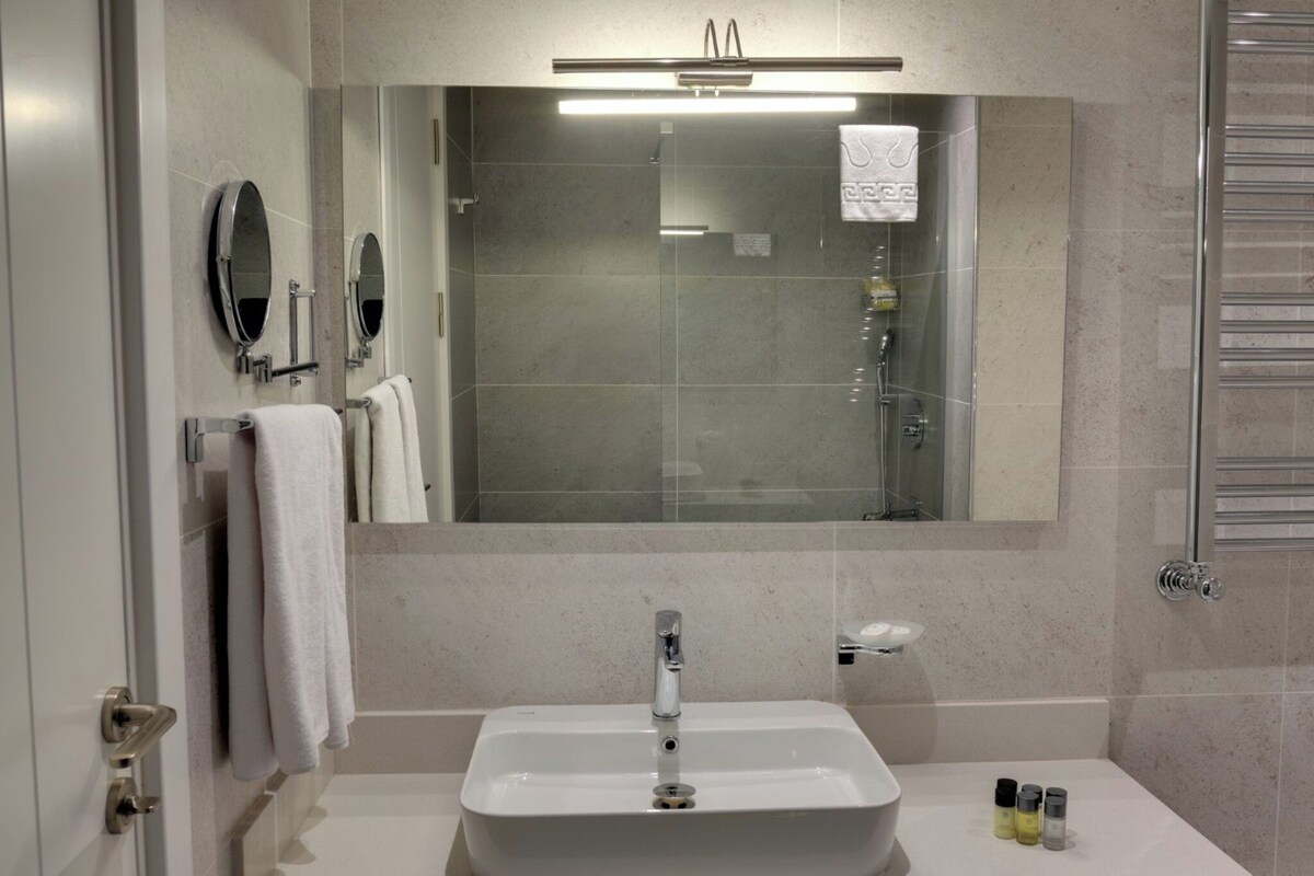 Un bagno moderno con uno specchio grande, un lavandino bianco e una cabina doccia in vetro.